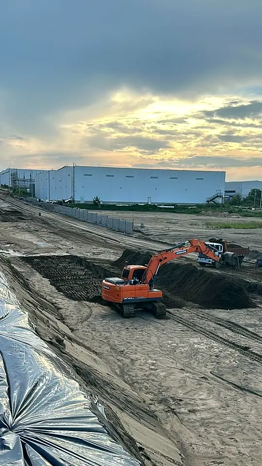 Excavadora Doosan haciendo movimiento de tierra junto a bodegas